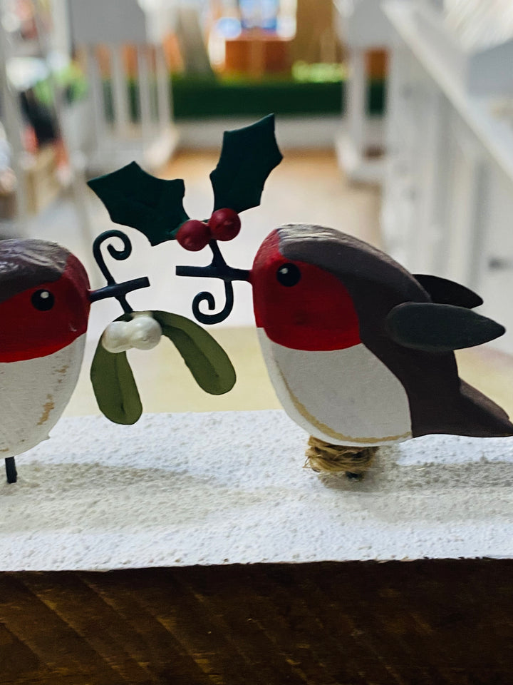 Decorative wooden birds with mistletoe on a white surface.