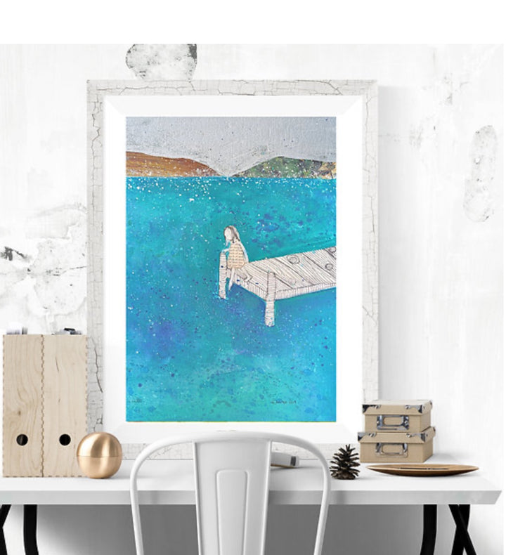 Framed artwork of a person sitting on a dock by a body of water, displayed on a white wall.