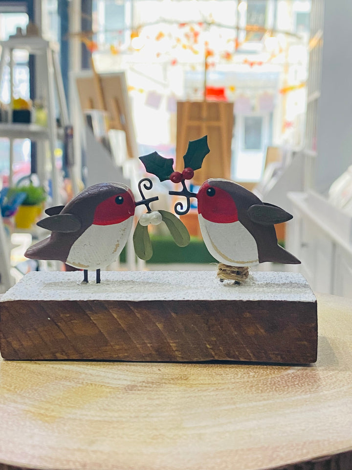 Decorative wooden figurine of two birds with holly leaves on a wooden base.