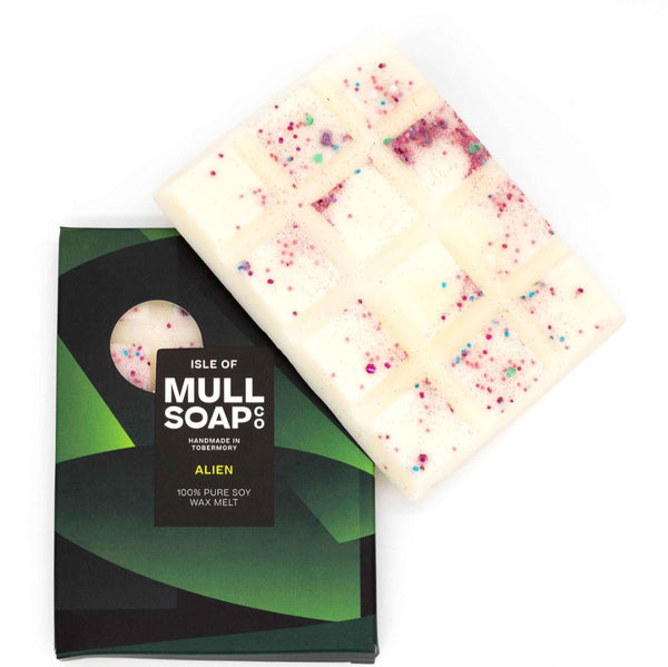 Alien wax melt  with colorful sprinkles next to its packaging on a white background